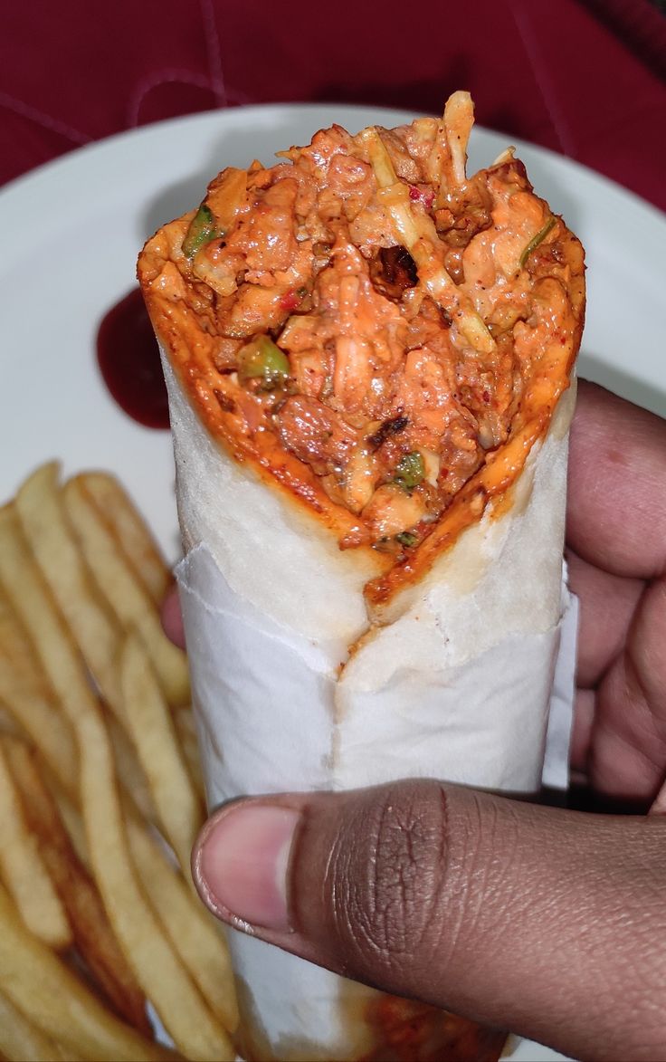 a hand holding a roll filled with food next to french fries on a white plate