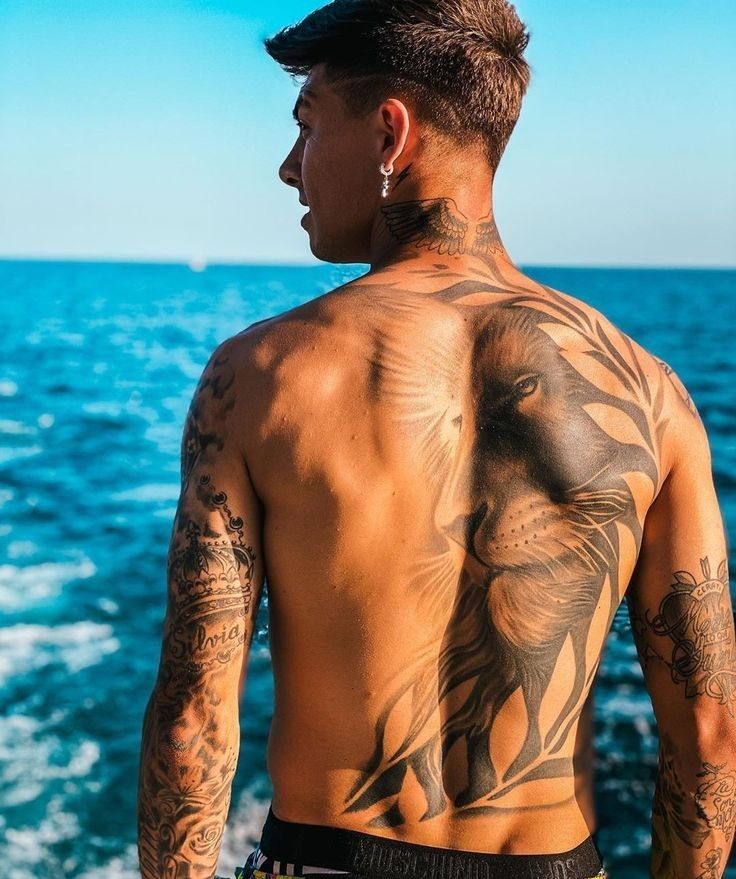 a man with tattoos on his back standing next to the ocean