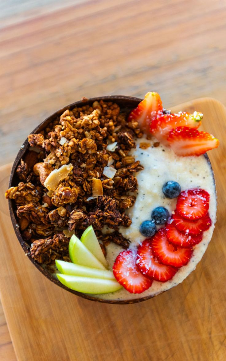 a bowl filled with granola and fruit on top of a wooden cutting board