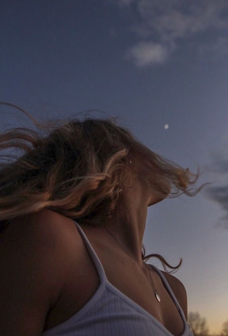 a woman with her hair blowing in the wind at sunset or dawn, looking up into the sky