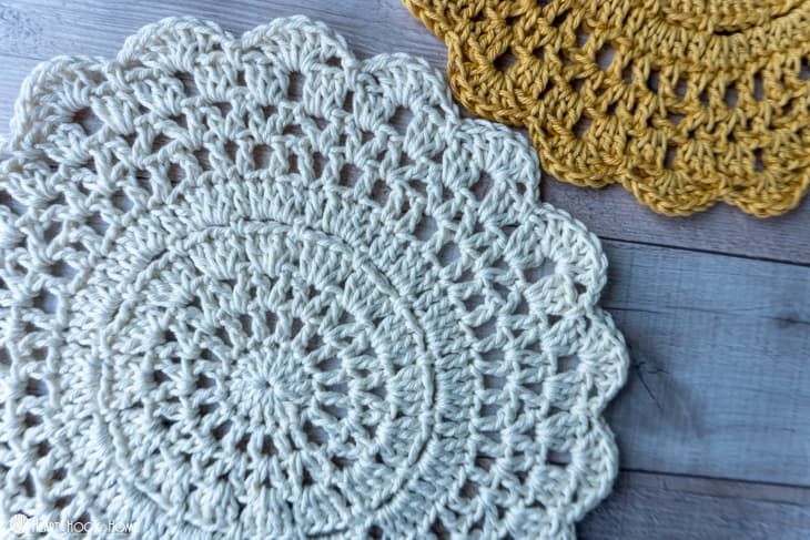 two crocheted doily are sitting on a wooden surface, one is yellow and the other is white