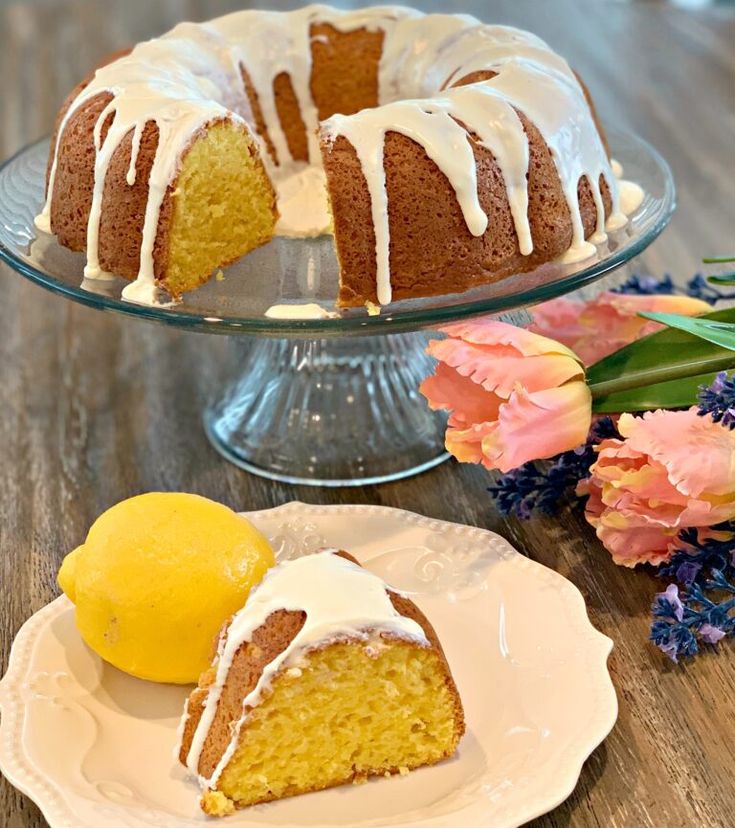 a bundt cake with white icing on a plate next to a lemon slice