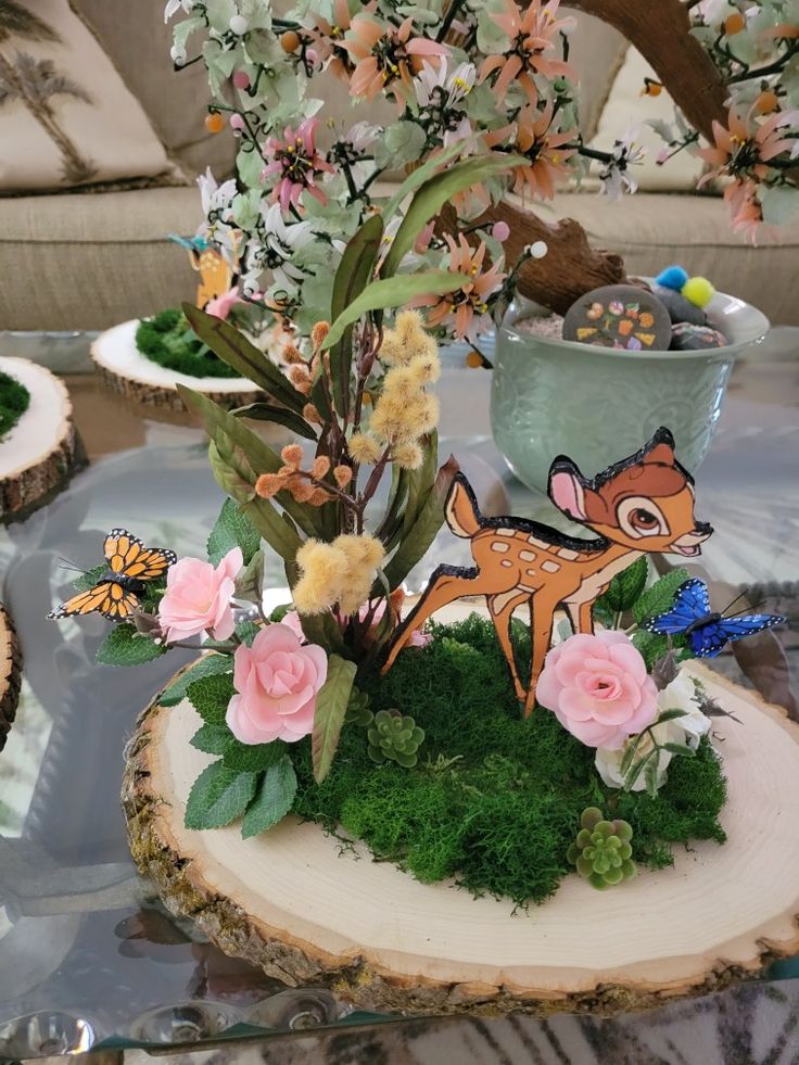 a glass table topped with flowers and fake animals on top of moss covered wood slices