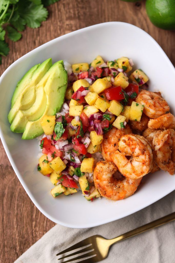 a white bowl filled with shrimp, pineapple salsa and avocado next to a fork