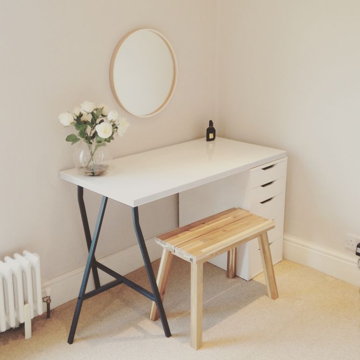 a white desk and stool in a small room with a round mirror on the wall