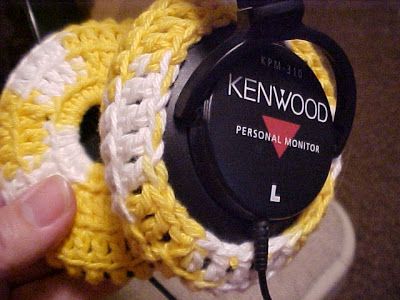 a person holding up a yellow and white crochet headphone case with the words kenwood on it