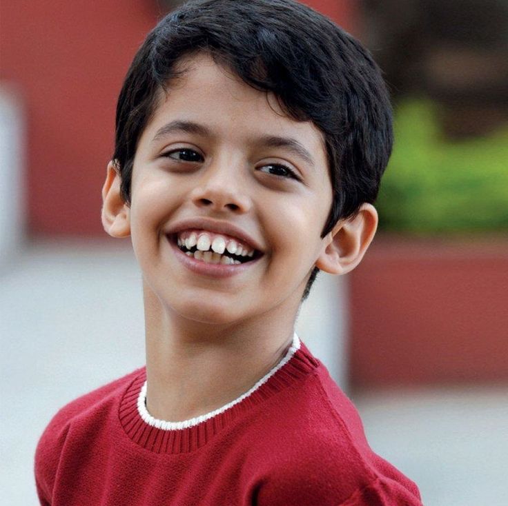 a young boy smiling and wearing a red shirt