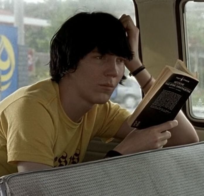 a young man sitting in the back seat of a car reading a book while holding his head up