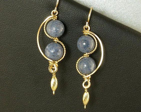 two blue beads are hanging from gold hoops on a black leather surface with a white background