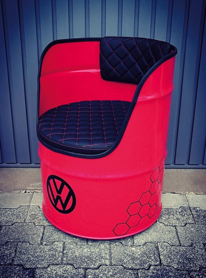 a red and black car seat sitting on top of a metal barrel next to a building