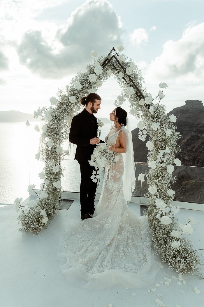 a bride and groom standing under an arch with white flowers on the ground next to each other