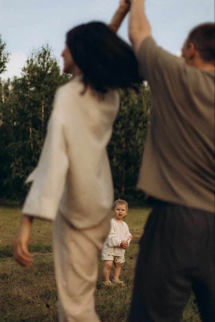 a man and woman are playing frisbee with a child in a field near trees