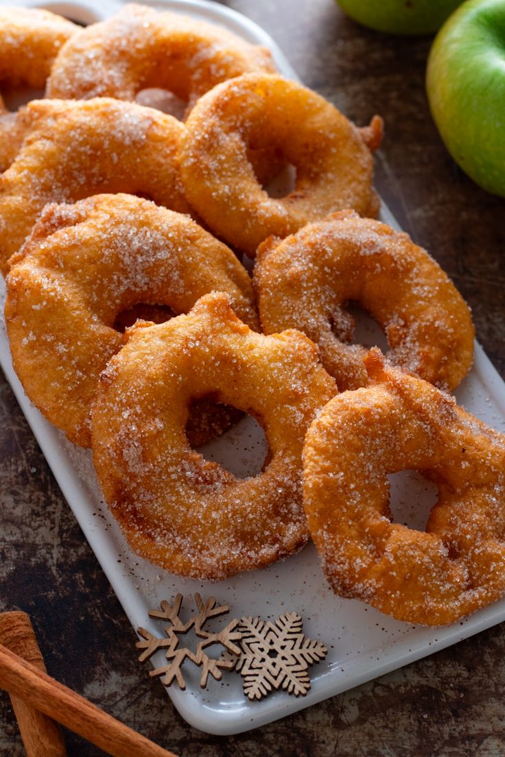 some sugared doughnuts are on a tray next to apples and cinnamon sticks