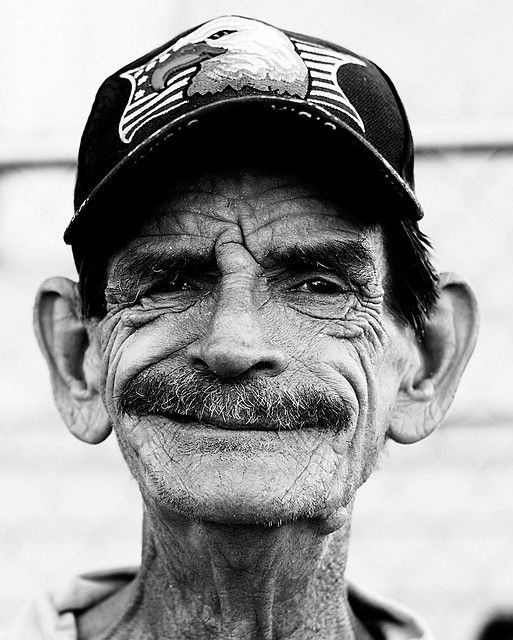 an old man with a mustache and a baseball cap on his head is looking at the camera