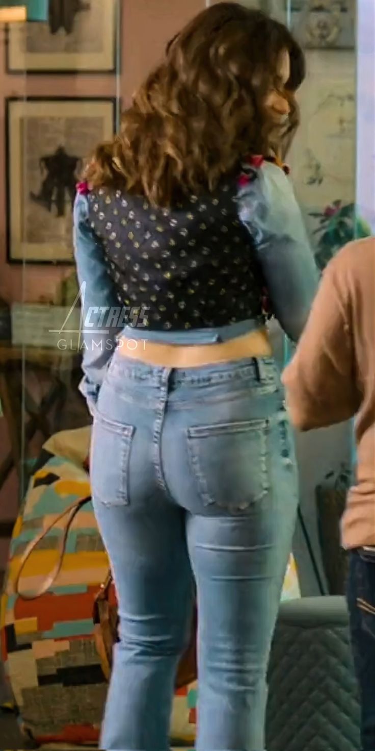 a woman standing in front of a mirror wearing high waisted jeans and a polka dot top