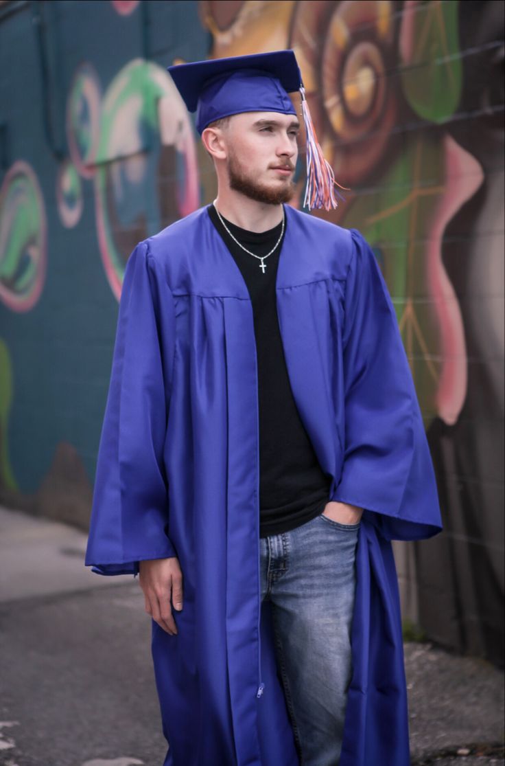 a man wearing a blue graduation gown standing in front of a graffiti wall