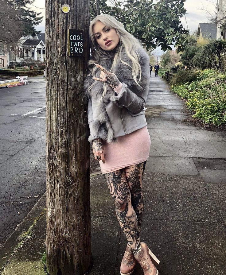 a woman standing next to a tree with tattoos on her arms and leggings