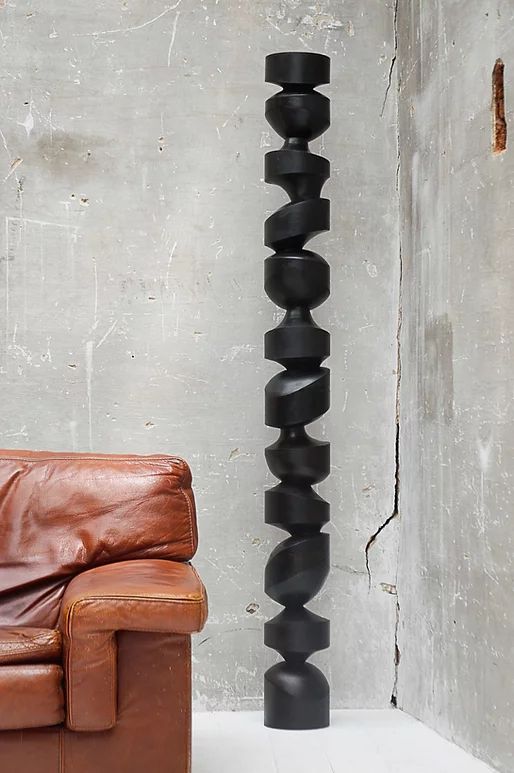 a brown leather chair sitting next to a tall black sculpture