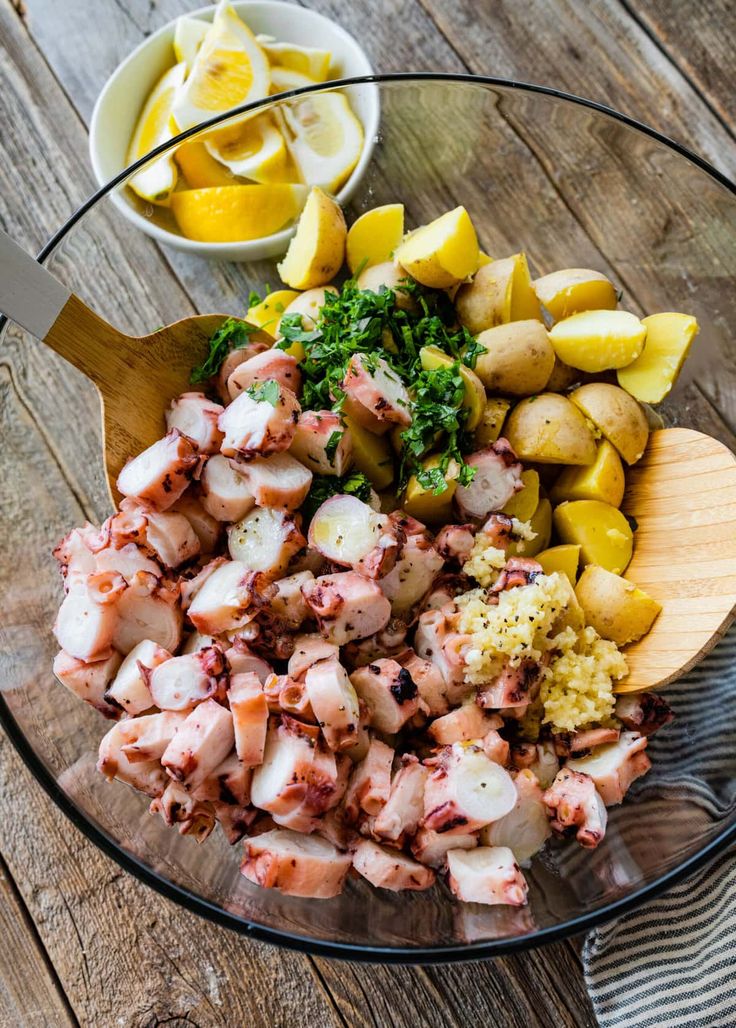 a glass bowl filled with different types of food on top of a wooden table next to lemon wedges