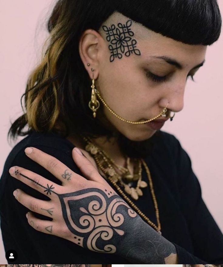 a woman with tattoos and piercings on her face is looking down at her hand