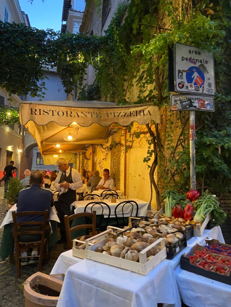 people sitting at tables in front of an outdoor restaurant with food on the outside table