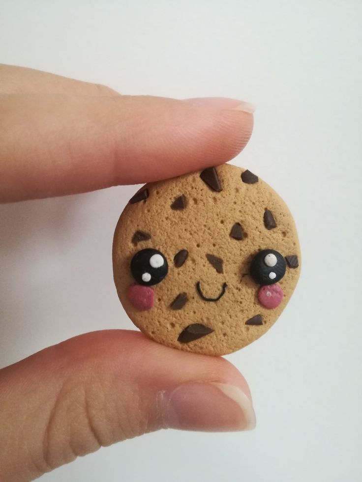 a hand holding a cookie with googly eyes and a smile on it's face