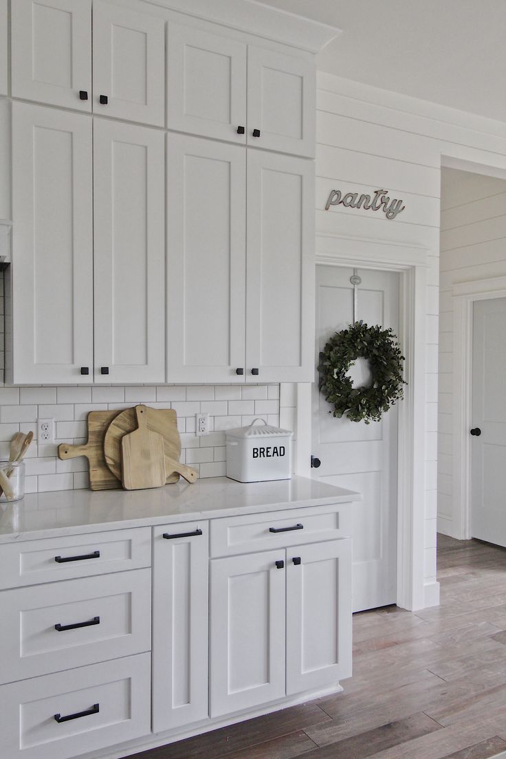 a kitchen with white cabinets and wood flooring is pictured in this image, there are wreaths on the wall