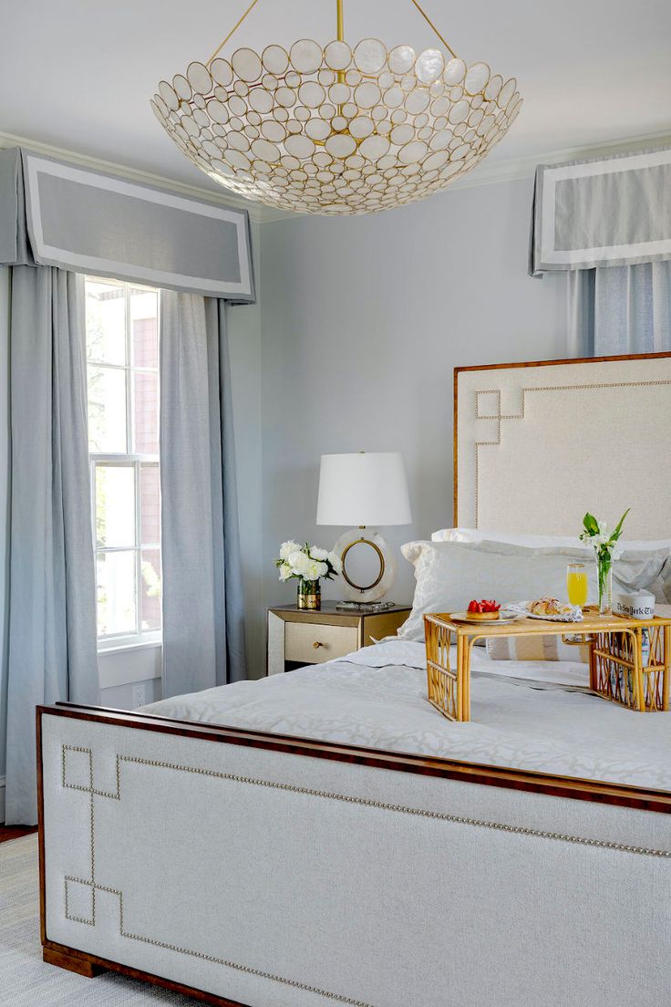 a white bed sitting in a bedroom under a chandelier next to a window