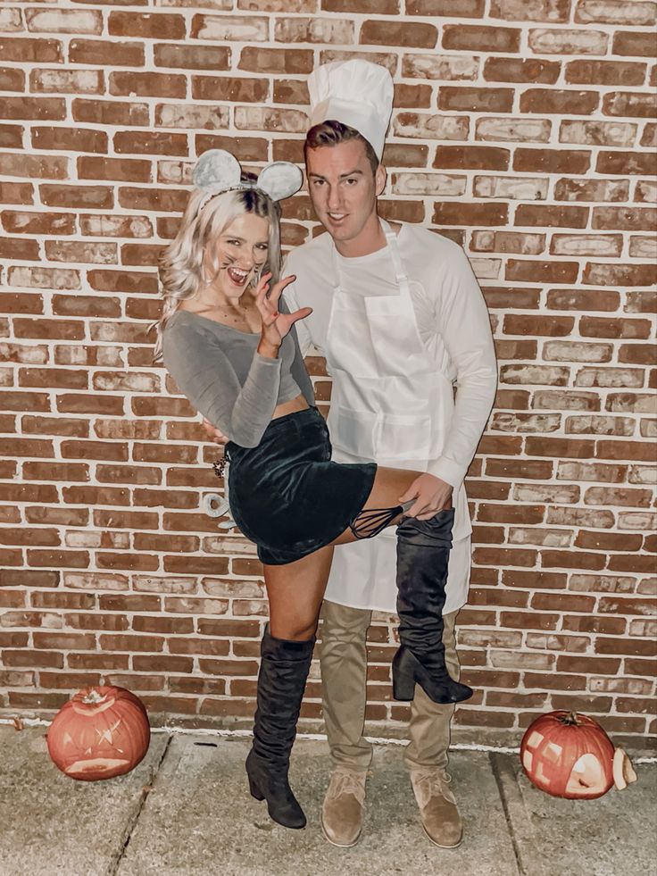 a man and woman dressed in costumes standing next to each other near pumpkins on the ground