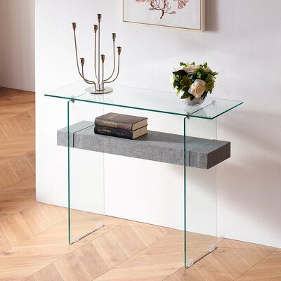 a glass table with a book on it in front of a white wall and wooden floor