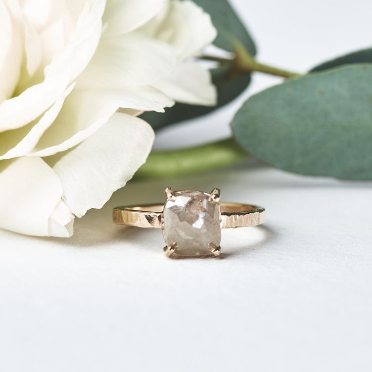 a close up of a flower and a ring on a white surface with flowers in the background