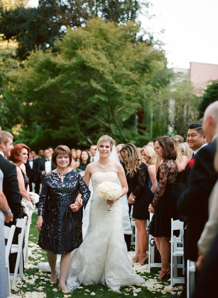 a bride and her mother walking down the aisle at their wedding ceremony in front of an audience