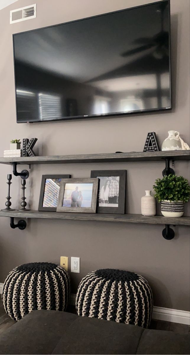 a flat screen tv mounted to the side of a wall above two black and white ottomans