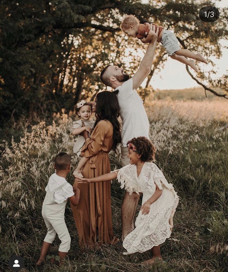 a group of people standing around each other in a field with trees and grass behind them