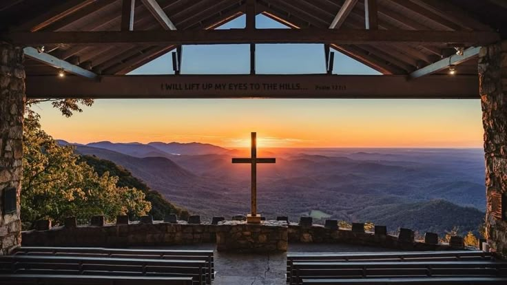 the sun is setting behind a cross on top of a hill with mountains in the background