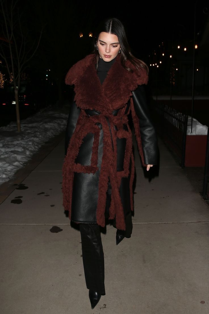 a woman walking down a sidewalk at night wearing a fur coat and leather pants with black boots