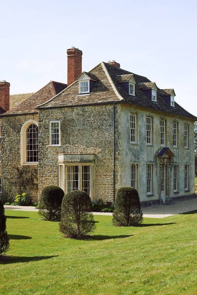 an old stone house with hedges in the front yard