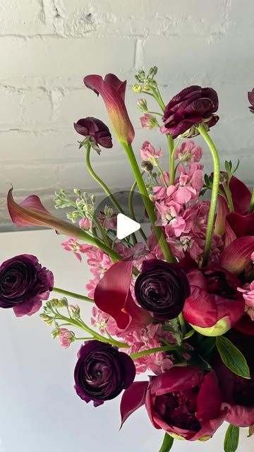 a vase filled with purple and red flowers on top of a white countertop next to a brick wall