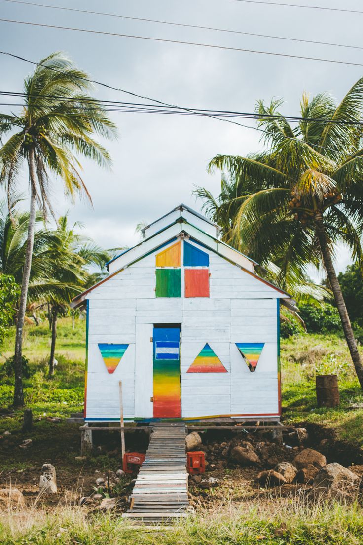 a white house with rainbow painted on the side and steps leading up to it, surrounded by palm trees