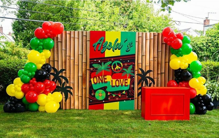 an outdoor party with balloons and decorations on the grass in front of a bamboo fence