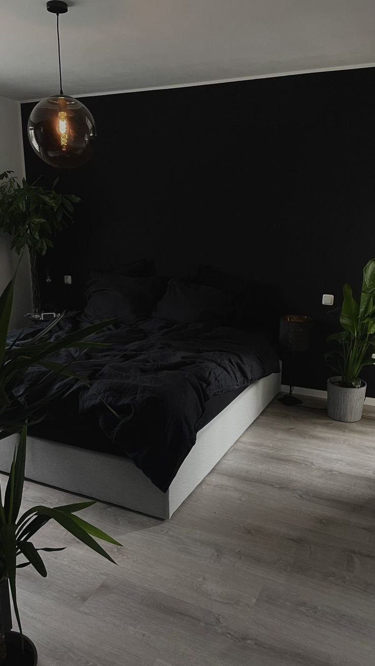 a bedroom with black walls and wooden flooring is pictured in this image, there are plants on either side of the bed