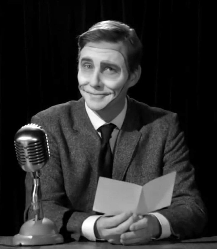 a man sitting at a table in front of a microphone and holding a piece of paper