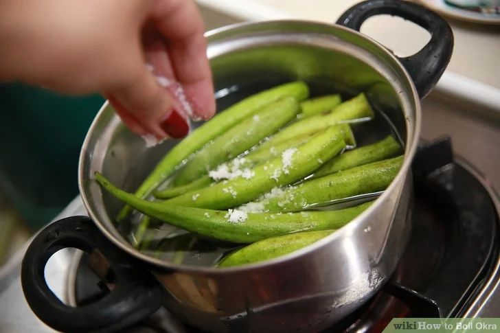 a person is cooking green beans in a pot on the stove top with salt sprinkled on them