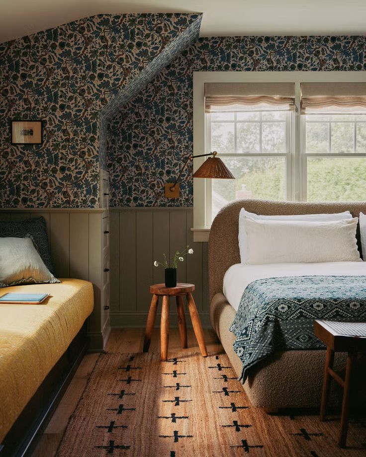 a bed sitting next to a window in a bedroom under a slanted ceiling with blue and green wallpaper