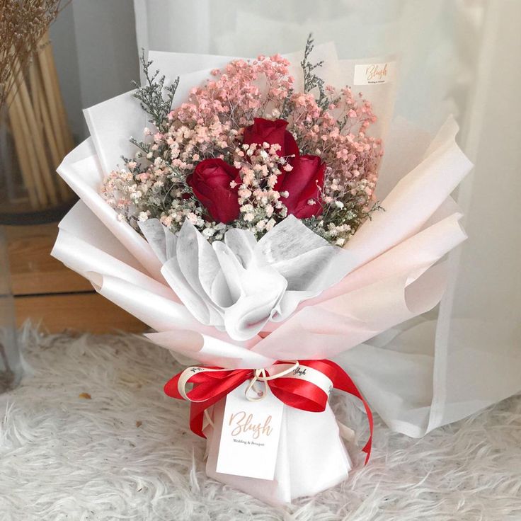 a bouquet of flowers is wrapped in white paper and tied with a red ribbon on the floor