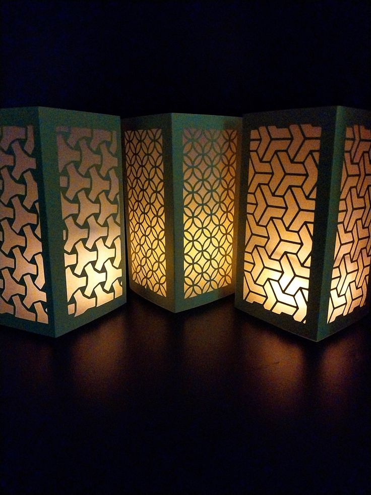 four paper lanterns sitting next to each other on top of a wooden table with one lit up