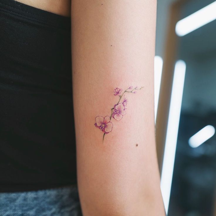 a woman's arm with a small pink flower tattoo on the left side of her arm