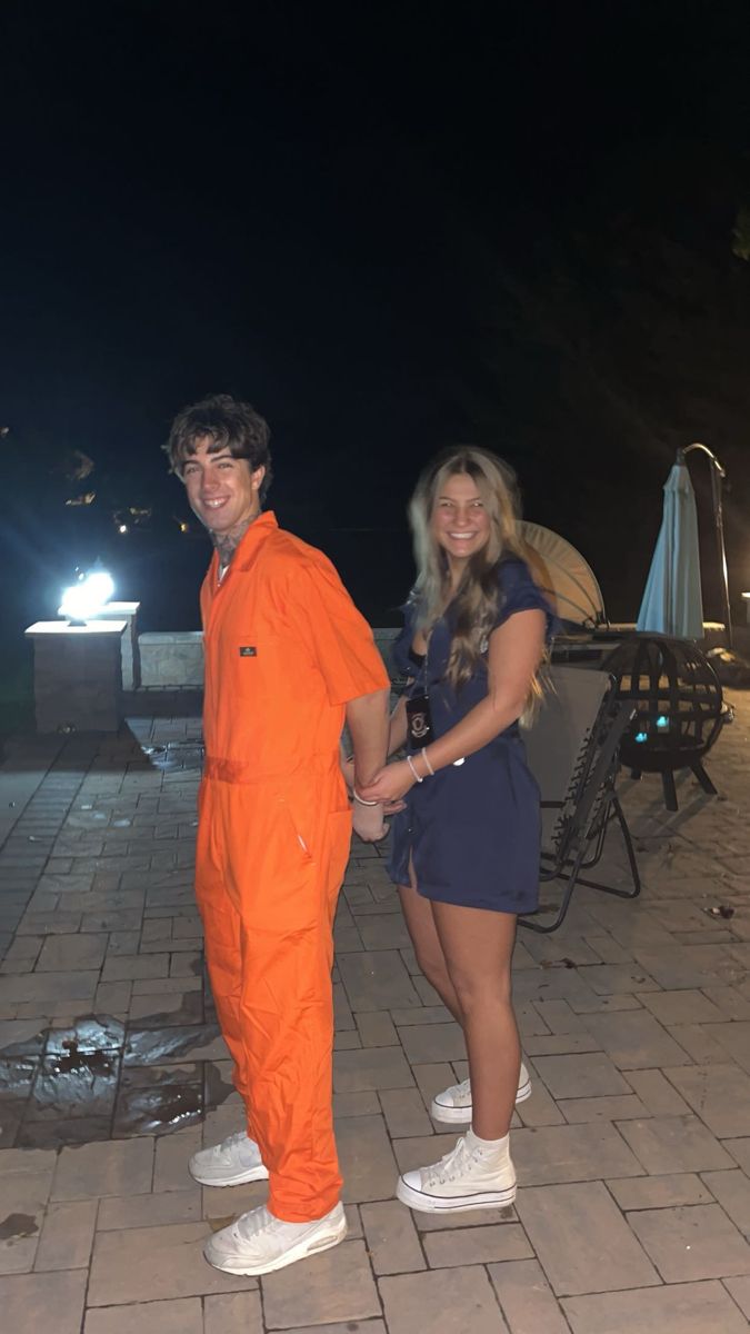 two people in orange jumpsuits standing next to each other on a brick patio