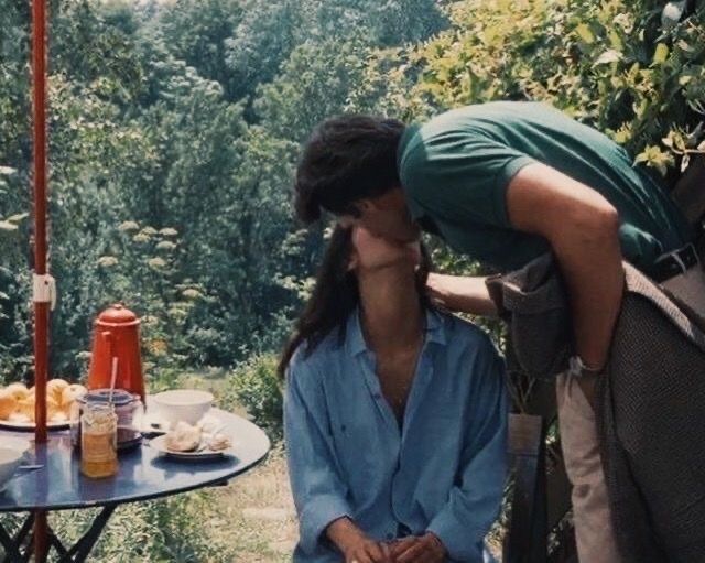 a man kissing a woman on the cheek in front of a table with food and drinks