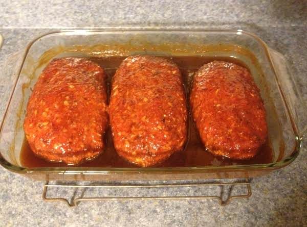 three meat patties in a glass dish on a counter top, ready to be cooked